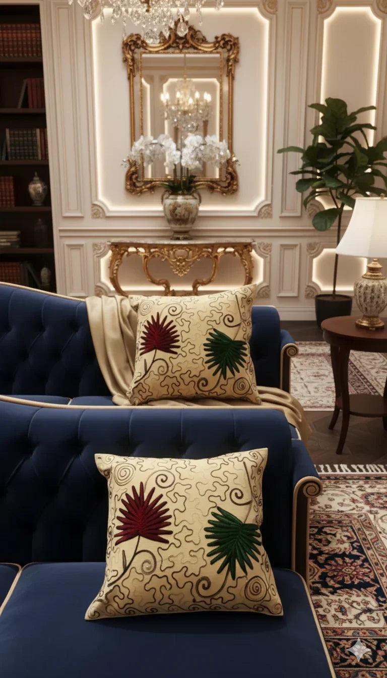 Decorative throw pillow with red and green floral embroidery on beige swirl background, styled on gray sofa