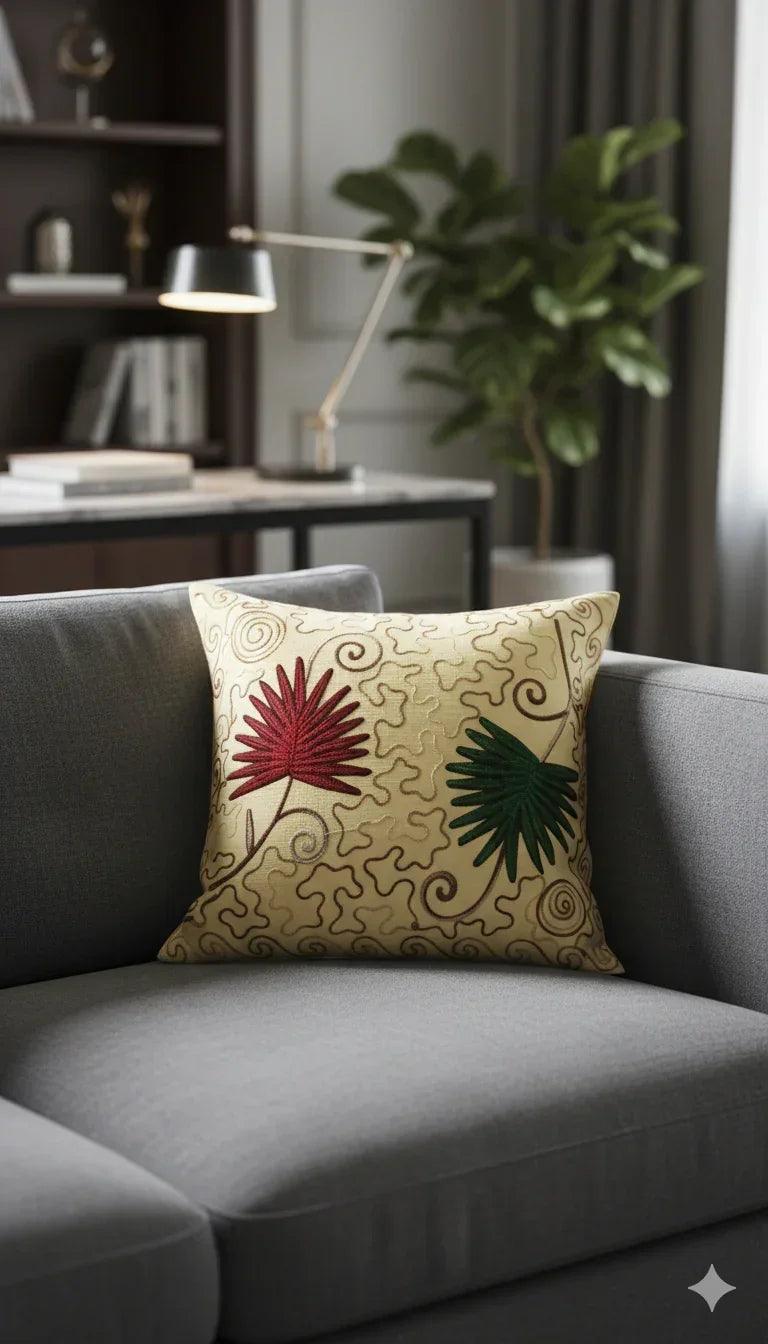 Decorative throw pillow with red and green floral embroidery on beige swirl background, styled on gray sofa