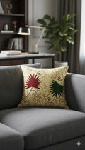 Decorative throw pillow with red and green floral embroidery on beige swirl background, styled on gray sofa