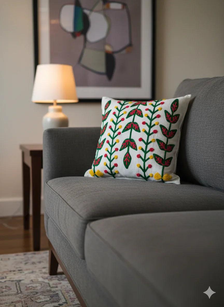 White embroidered pillow with green leaves and red yellow flowers on gray sofa, modern living room decor