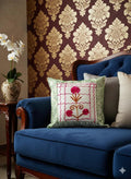 Embroidered floral cushion on blue velvet sofa with damask wallpaper and orchid vase