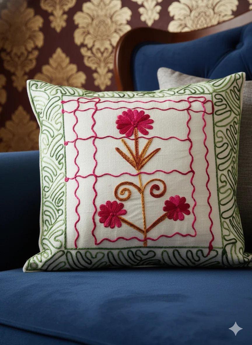 Embroidered floral pillow with pink flowers and green border on blue sofa, decorative home accent