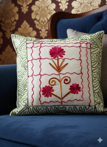Embroidered floral pillow with pink flowers and green border on blue sofa, decorative home accent
