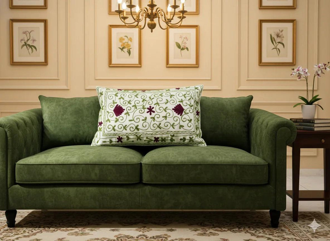 Embroidered floral throw pillow with green vines and burgundy flowers on cream fabric, styled on green sofa