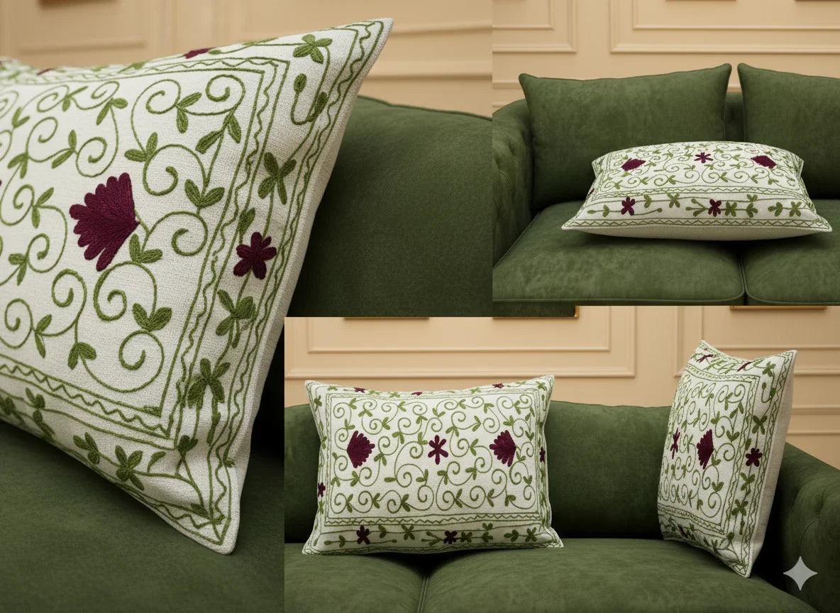 Embroidered floral throw pillow with green vines and burgundy flowers on cream fabric, styled on green sofa